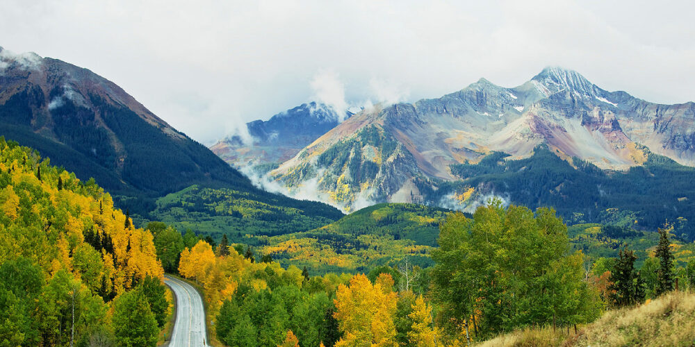 An impressive mountain scene with a road leading into the mountains of Telluride with colorful trees and mountain landscapes.