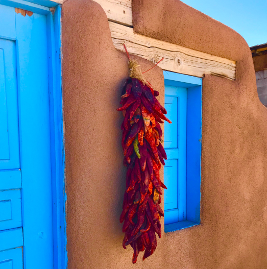 Adobe pueblo with blue windows and a hanging bunch of red hot chillies drying